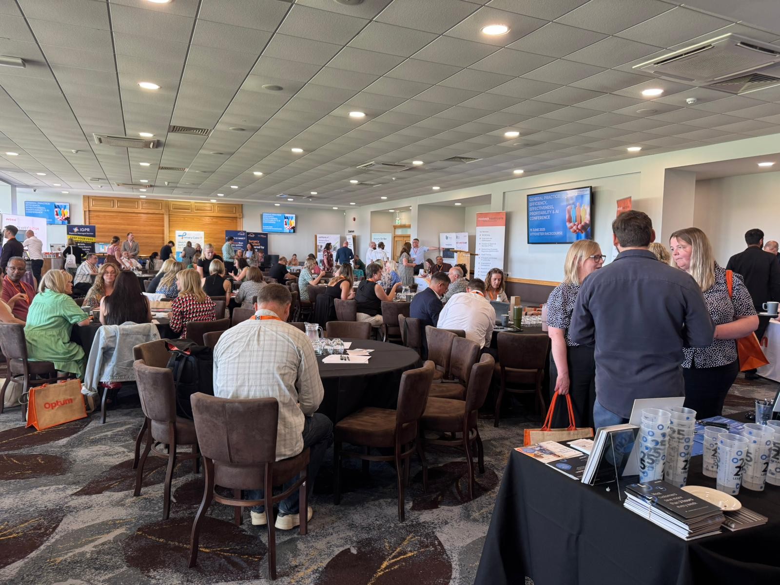 Wide shot of a room full of delegates in a conference suite whilst a member of the team stands at the front addressing the room.
