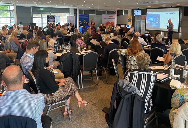 Wide shot of a room full of delegates in a conference suite whilst a member of the team stands at the front addressing the room.