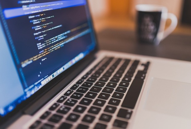 A close up of a laptop screen and keyboard with coding on the screen.