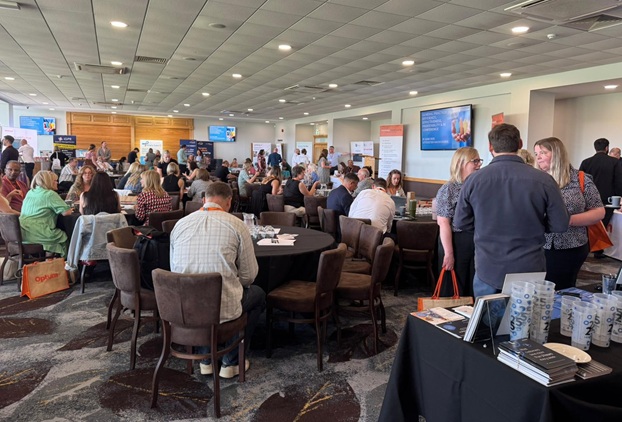 Wide shot of a room full of delegates in a conference suite whilst a member of the team stands at the front addressing the room.