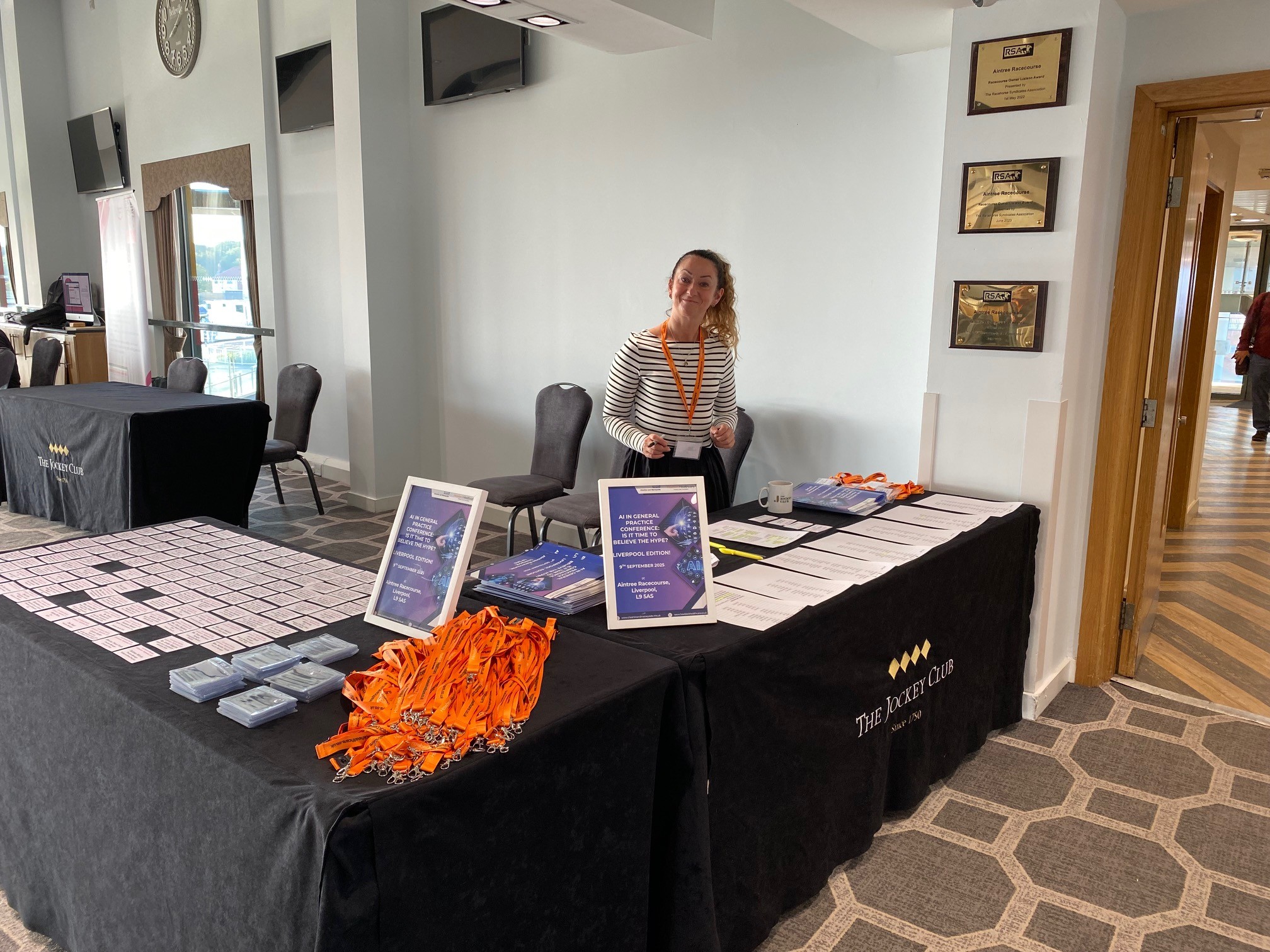 Nicki Laurie standung behind two tables in an L shape with registration sheets and badges are laid out.